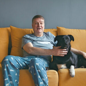 A person sits on a yellow sofa with a black dog